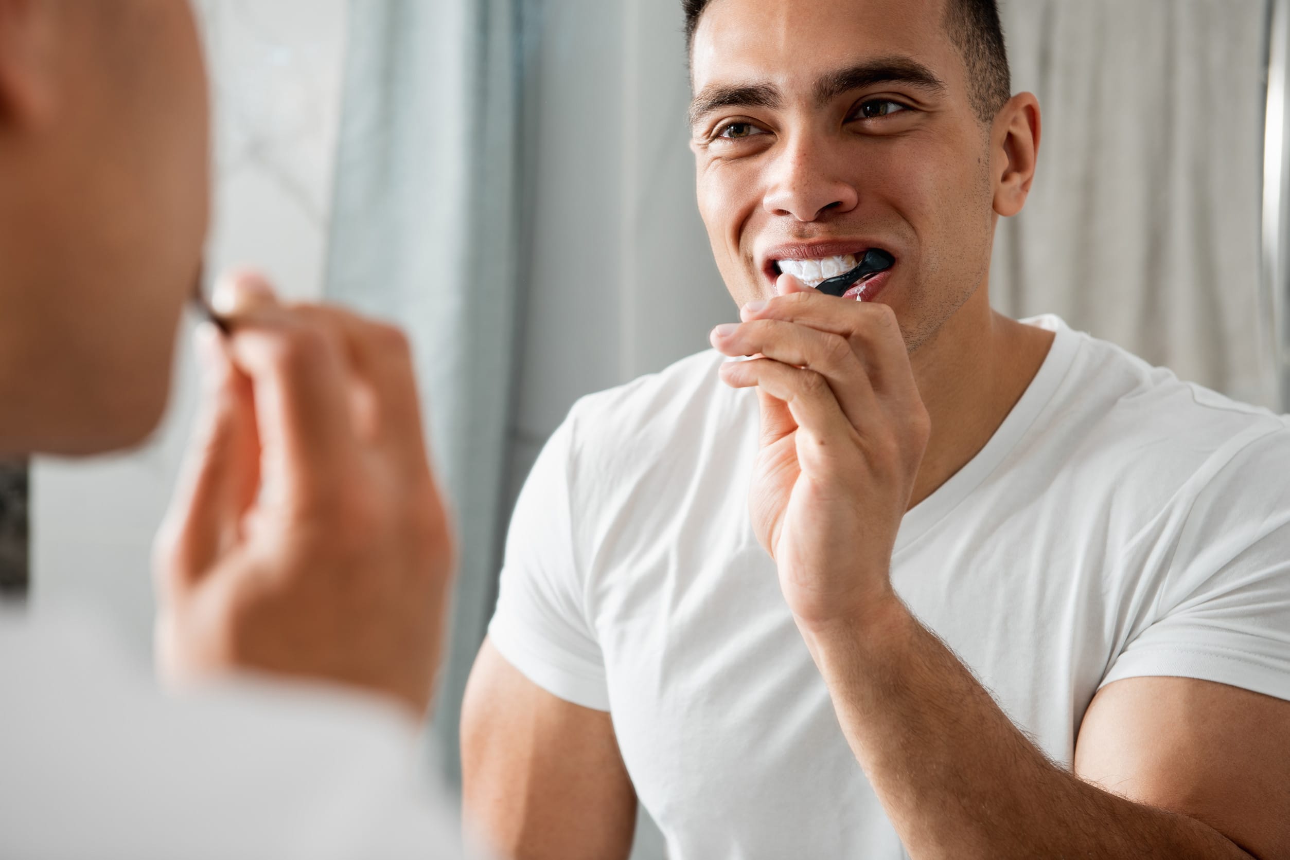Reflection of young smiling man brushing teeth