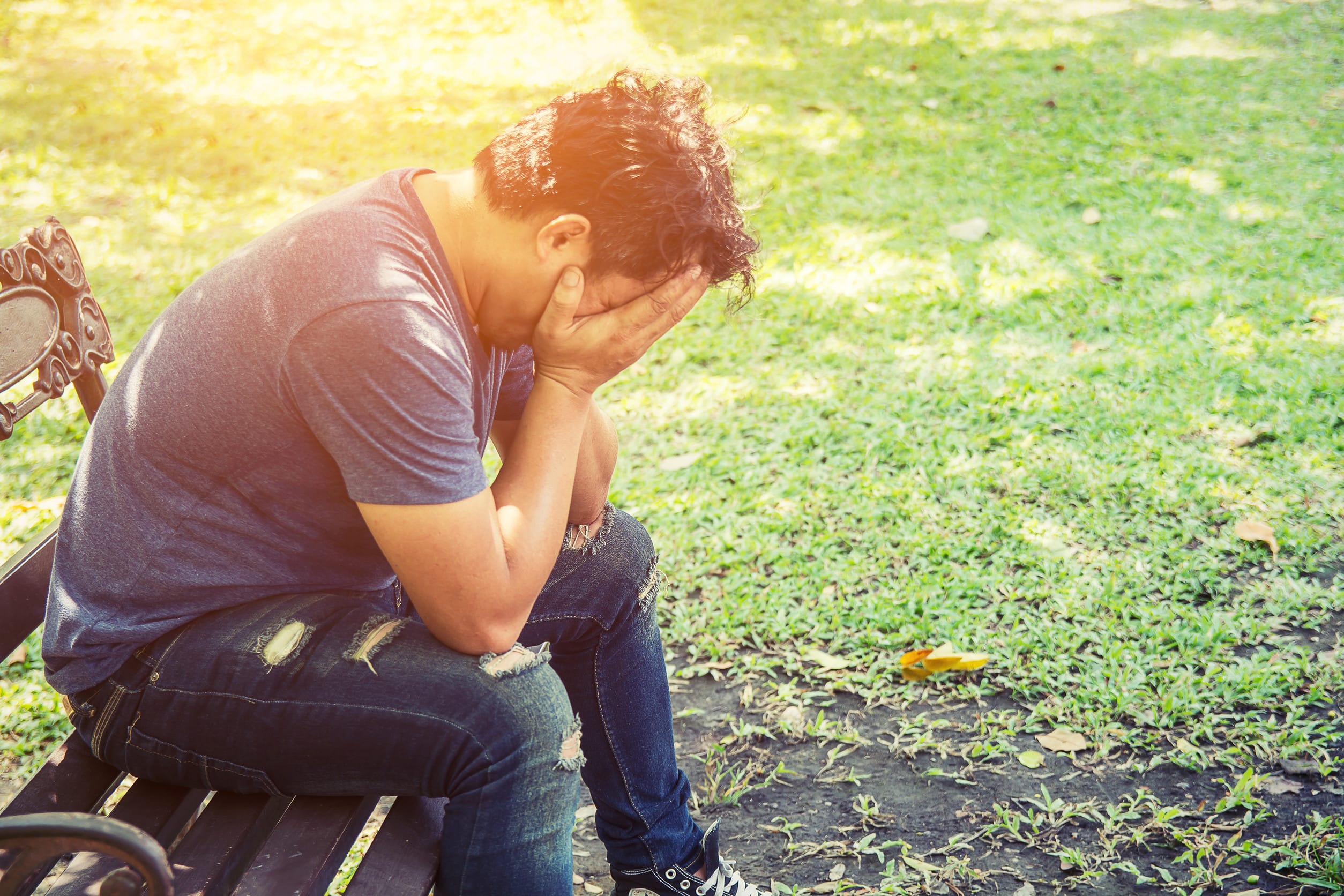 depressed man with head in his hands on a bench
