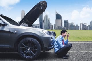 Man sitting in front of a car with the hood up
